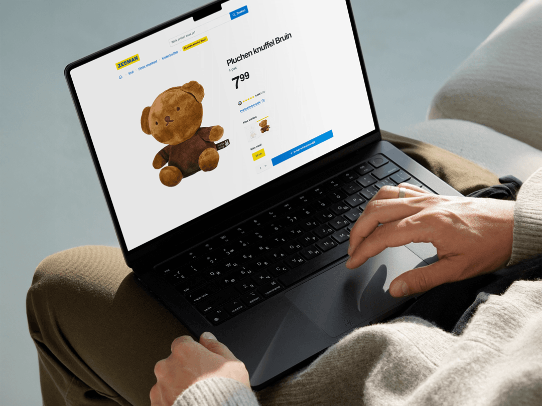 Person shopping online for a brown teddy bear on a laptop, displaying a product page with price and purchase options.